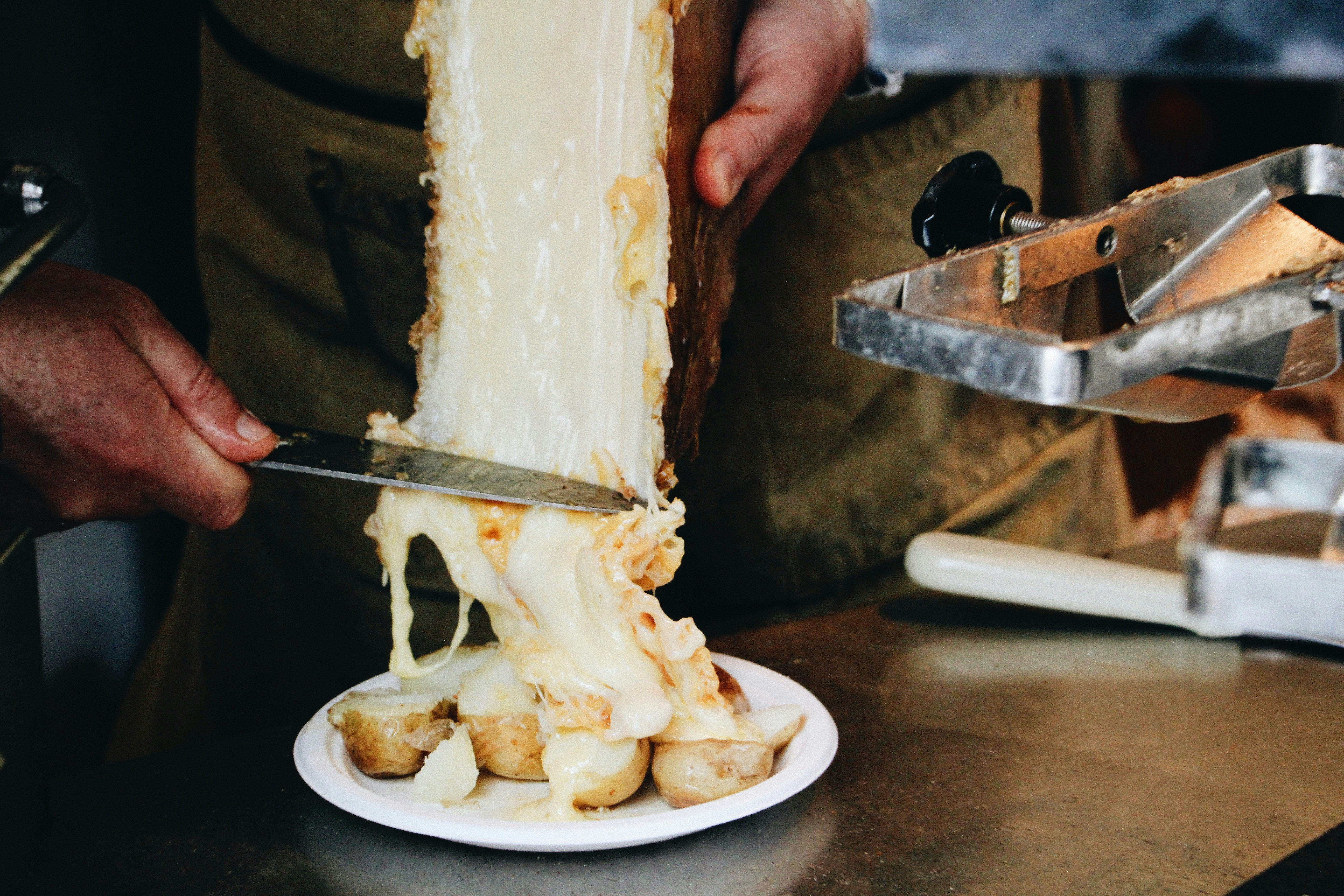 Melted raclette cheese being scraped over boiled potatoes